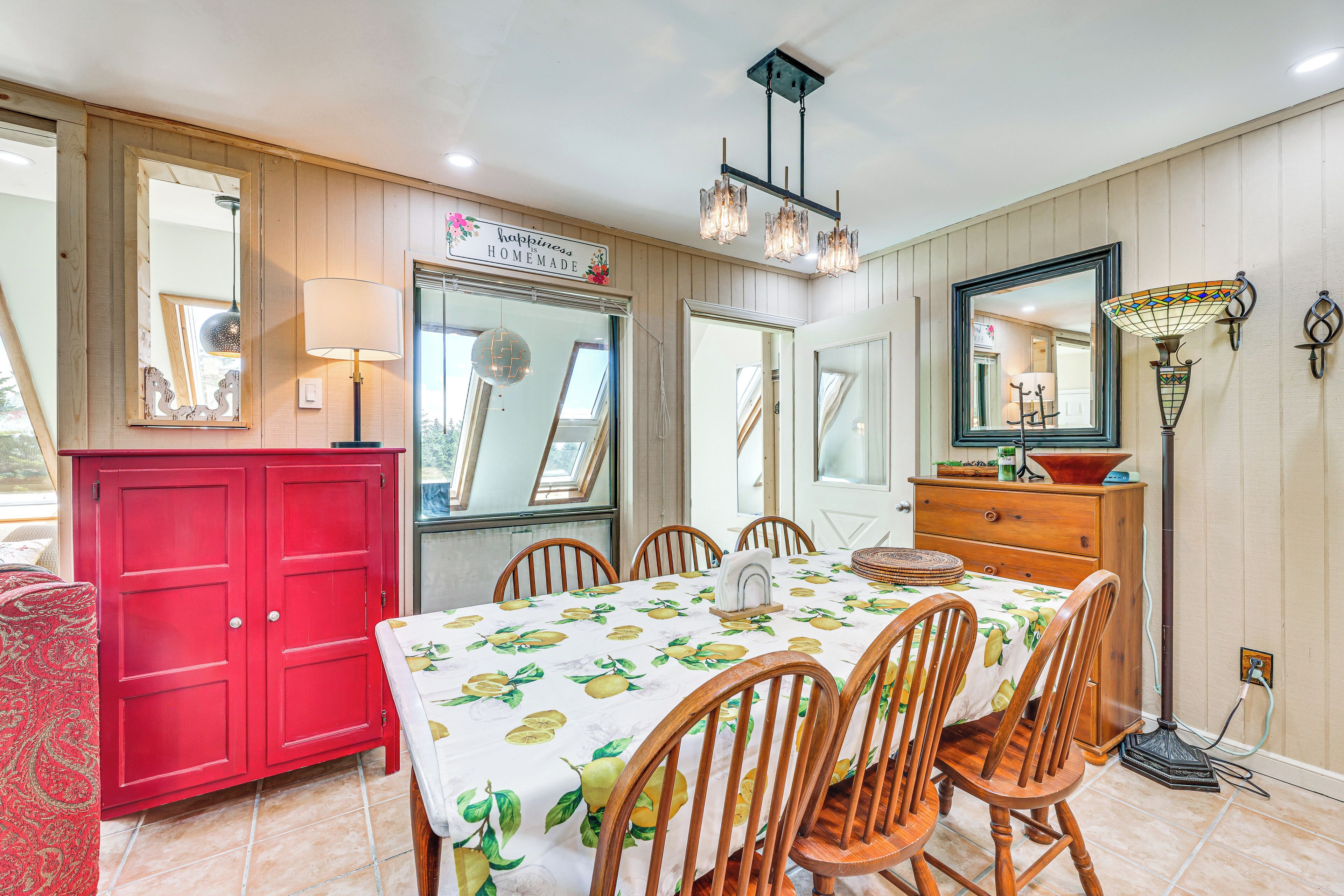 A dining area with a table set for four, surrounded by wooden chairs, a red cabinet, and a mirror above the table.