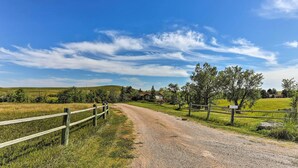 A gravel road leading to a house surrounded by fields and trees.