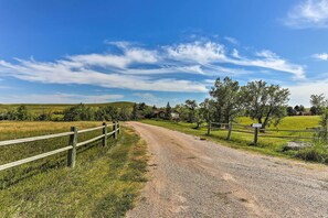 A gravel road leading to a house surrounded by fields and trees.