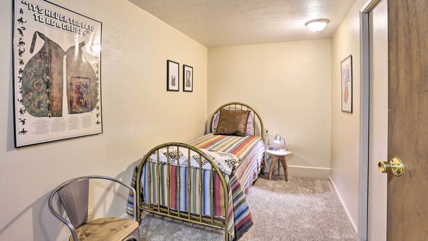 A bedroom with a metal bed frame, a striped bedspread, a small bedside table with a lamp, and a door with a brass handle.