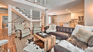 A spacious living area with a high ceiling, a staircase, a leather sofa, and a dining area. - Updated Condo Next to Burke Mountain Bike Trails! (East Burke)