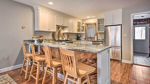 A modern kitchen with a large island, wooden bar stools, and stainless steel appliances. - Updated Condo Next to Burke Mountain Bike Trails! (East Burke)