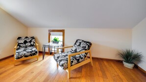 A room with two wooden chairs with black and white floral upholstery, a small table with a potted plant, and a view of a balcony with a plant. - Quaint Fredericksburg Studio w/ Shared Hot Tub (Fredericksburg)