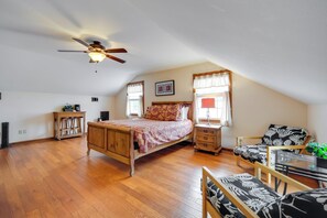 A bedroom with a wooden bed, a nightstand, a chair, a desk, a ceiling fan, and two windows with curtains. - Quaint Fredericksburg Studio w/ Shared Hot Tub (Fredericksburg)
