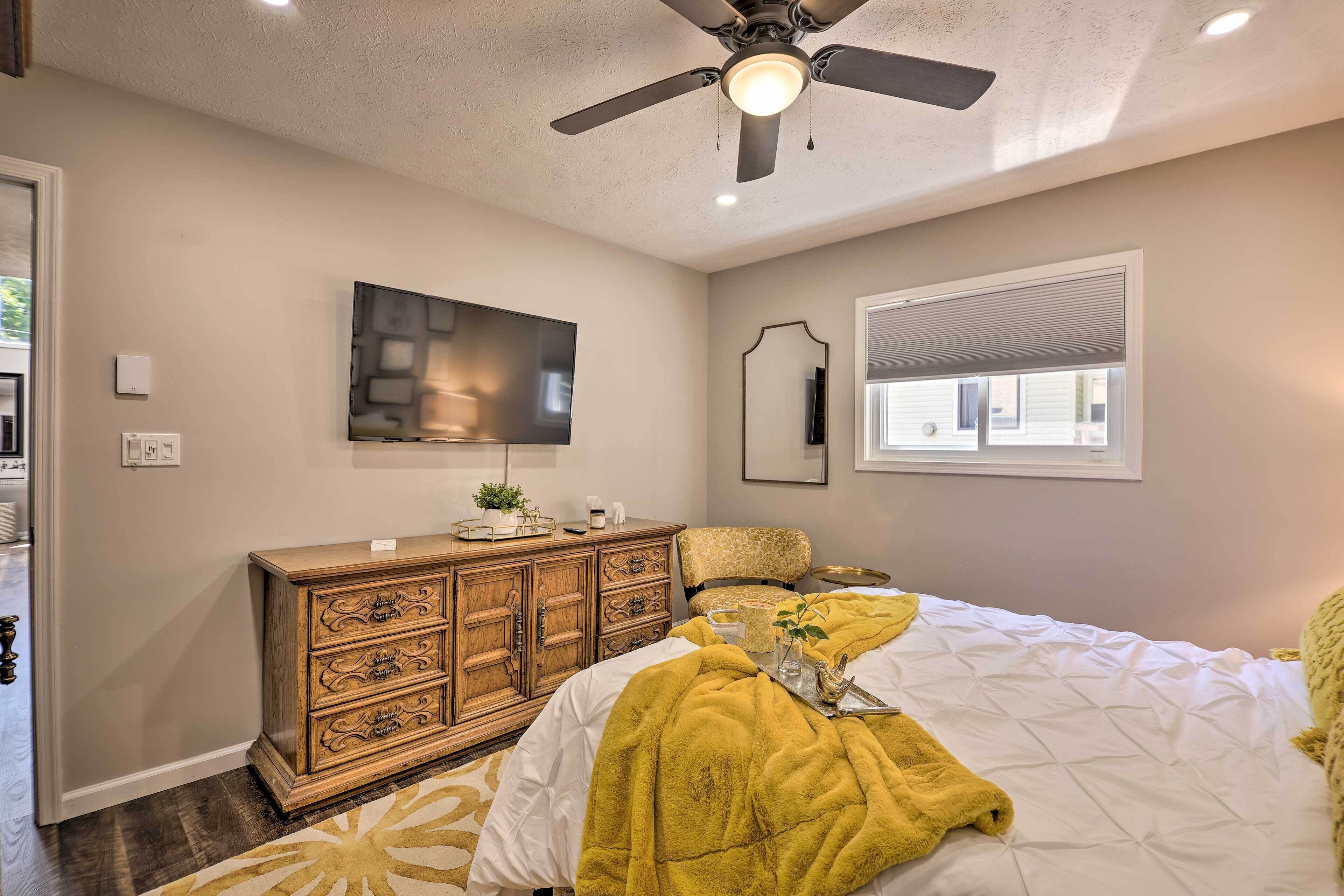 Une chambre à coucher avec un lit, un ventilateur de plafond, une commode, un téléviseur et une fenêtre.
