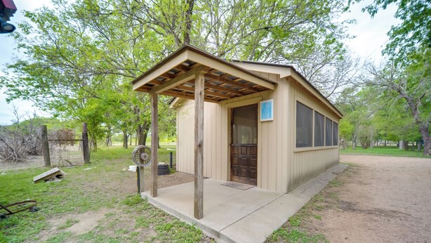 A small, single-story building with a wooden pergola entrance, a door, and a window. - Studio Cabin in Fredericksburg w/ Shared Hot Tub! (Fredericksburg)