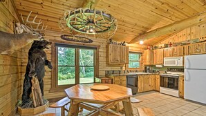A rustic cabin interior with wooden walls, a dining table, and a kitchen area. - Scenic Cabin on 2 Acres Near Lake Holcombe Marina! (Holcombe)