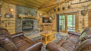 A log cabin interior with leather sofas, a stone fireplace, mounted animal heads, and a television. - Scenic Cabin on 2 Acres Near Lake Holcombe Marina! (Holcombe)