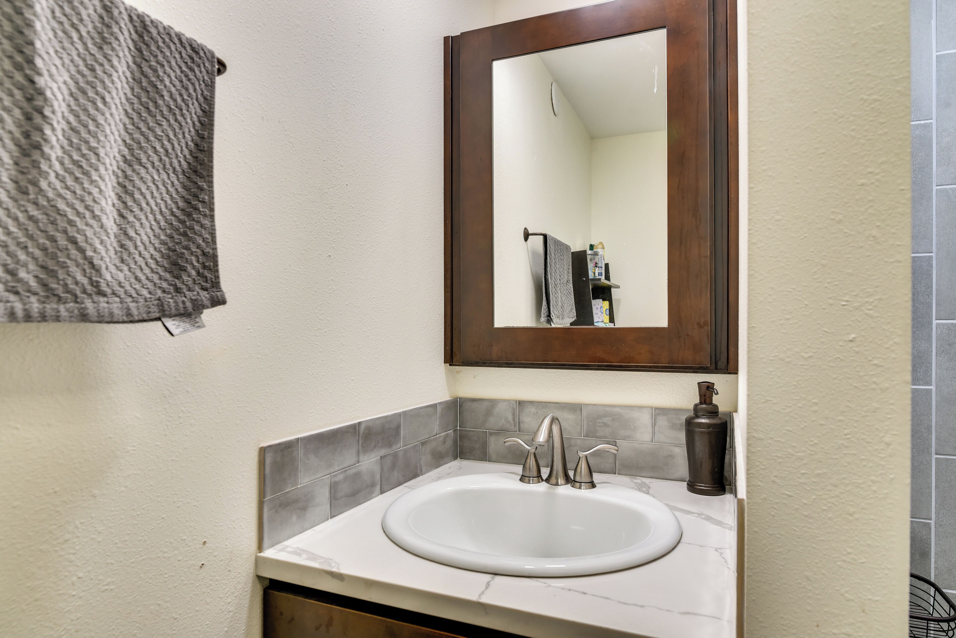 Een badkamer met een wit wastafelmeubel, een spiegel met houten lijst en een handdoek aan de muur.