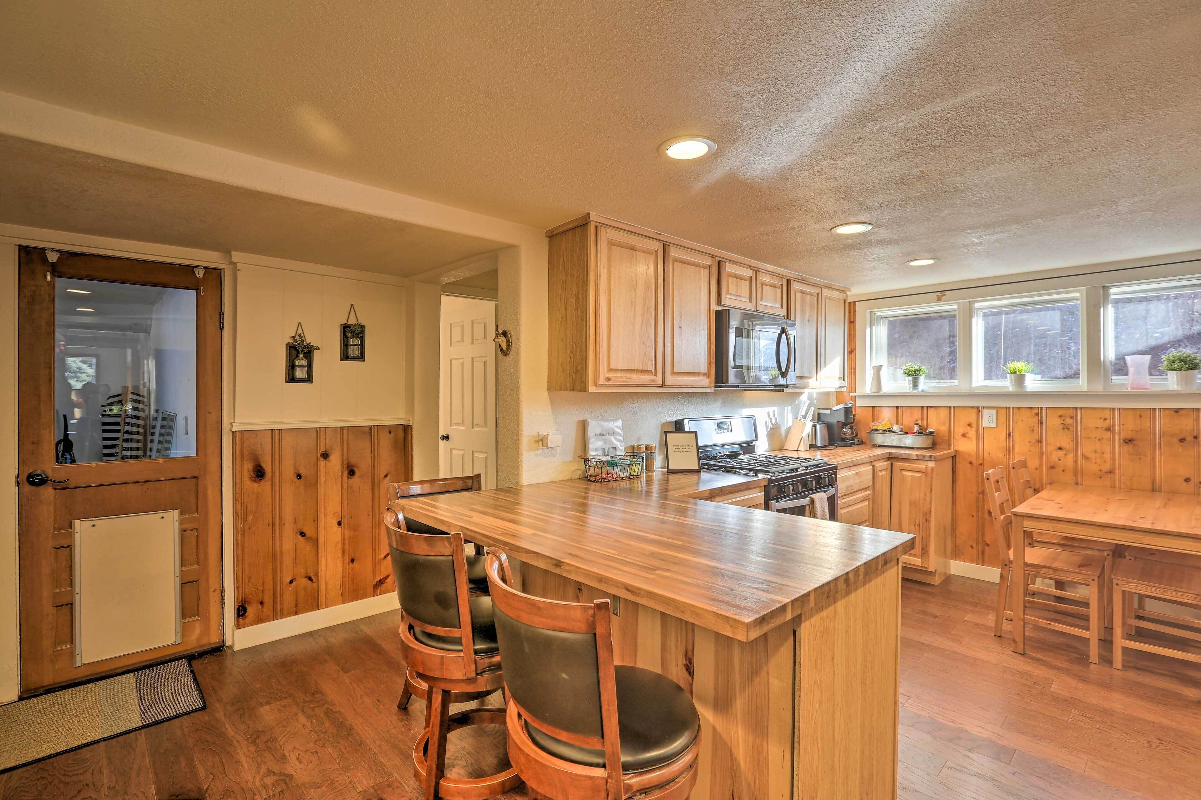 A kitchen with wooden cabinets, a central island with bar stools, a microwave, and a stove.