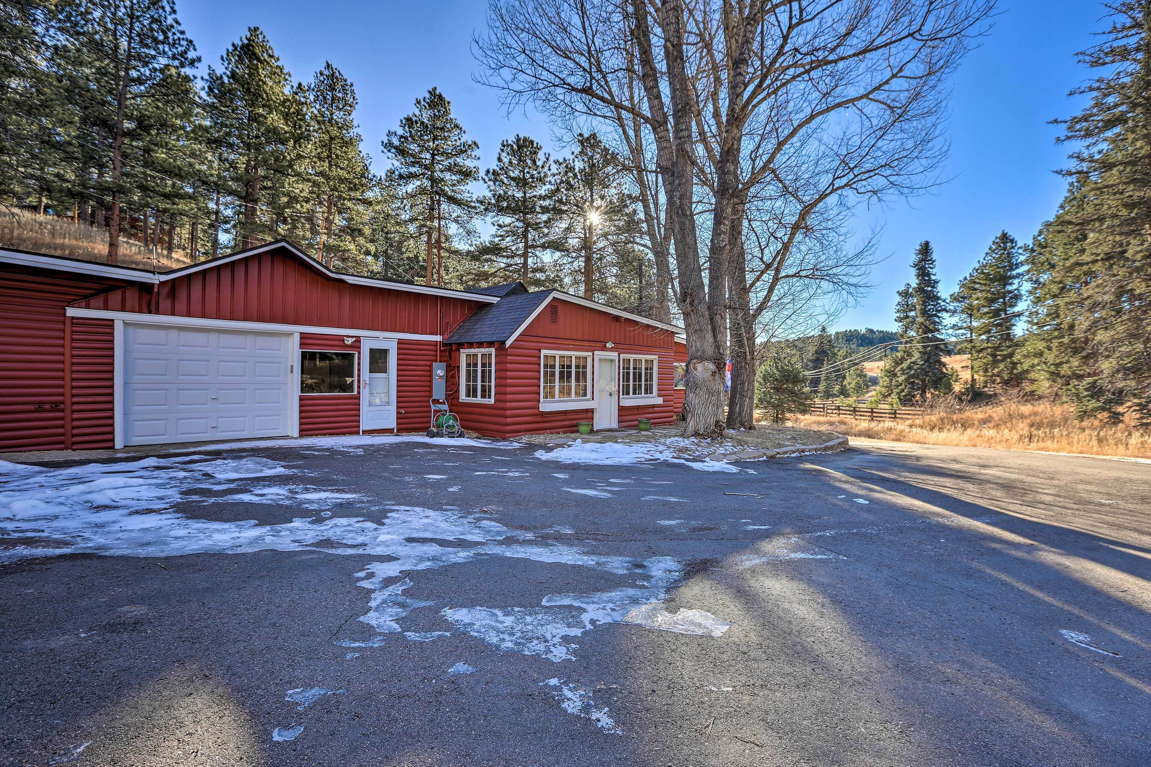 A red cabin with a garage, surrounded by trees and a clear sky.