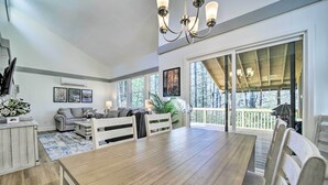A spacious dining area with a wooden table and chairs, a chandelier, and large windows offering views of the outdoors. - Sapphire Home w/ Grill & Pool Access (Sapphire)