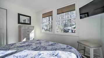 A bedroom with a bed, a dresser, a window with a view of trees and a car, and a TV mounted on the wall.