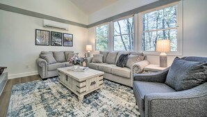 A living room with a sectional sofa, a coffee table, and a rug. There are two windows with a view of trees. - Sapphire Home w/ Grill & Pool Access (Sapphire)