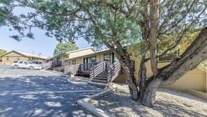 A motel with a parking lot, a tree in front of the building, and a white SUV parked. - Ruidoso Condo w/ Golf View ~ 17 Mi to Ski Apache! (Ruidoso)