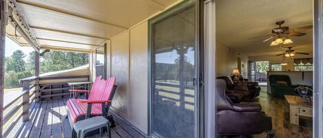 Une véranda avec des fauteuils Adirondack rouges, une petite table et une porte-fenêtre coulissante donnant sur un espace de vie intérieur comprenant un canapé, une table basse et des ventilateurs de plafond.
