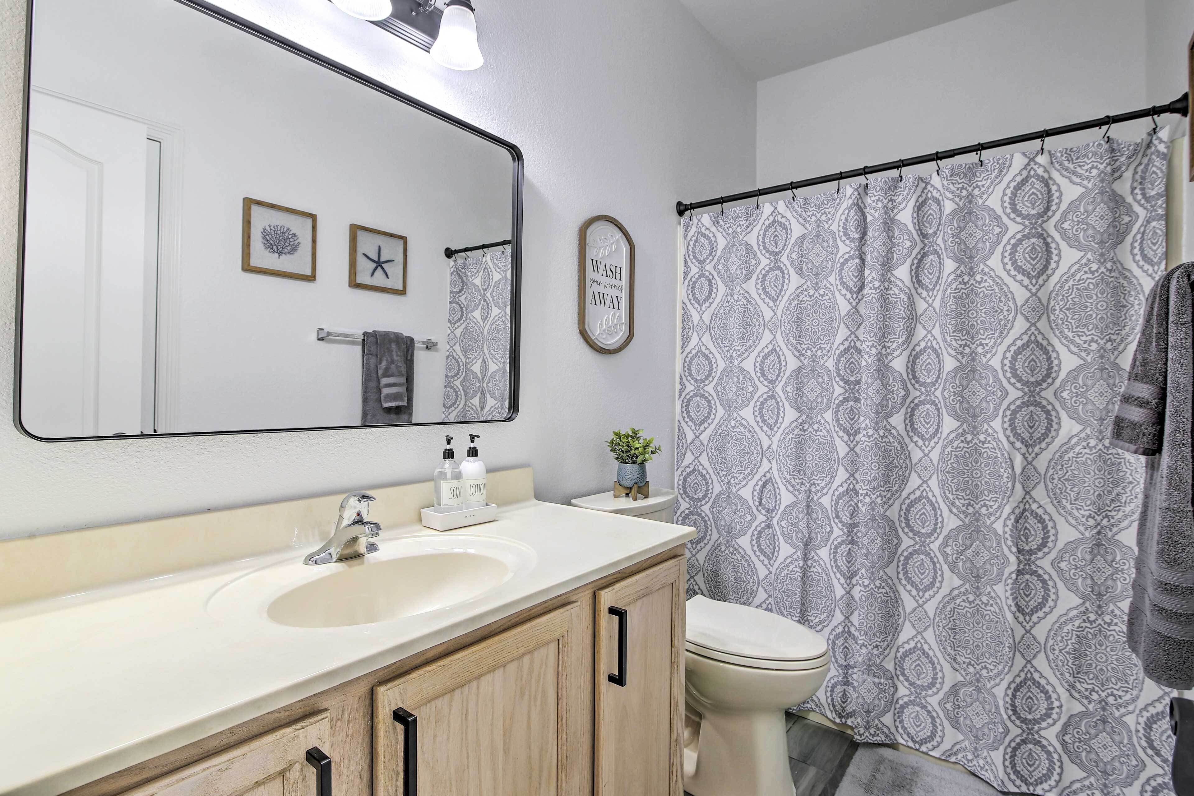 A bathroom with a white sink, a mirror, a toilet, and a shower curtain with a pattern.