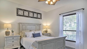 Une chambre à coucher comprenant un lit, deux tables de chevet, une fenêtre avec des rideaux et un cadre photo fixé au mur.