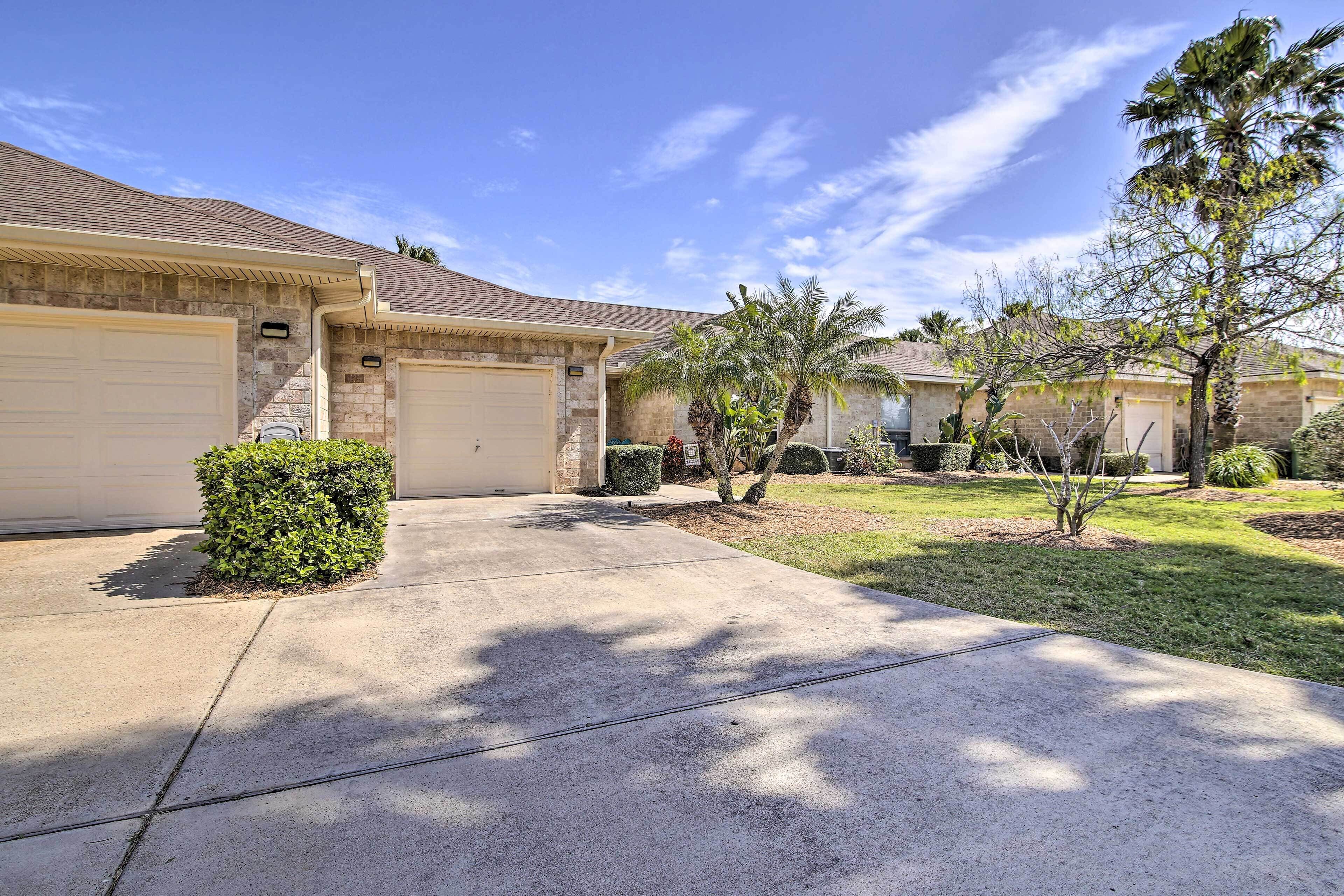 A residential driveway leading to a garage, surrounded by well-maintained lawns and small trees.
