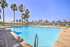 A swimming pool with clear blue water, surrounded by palm trees and lounge chairs.