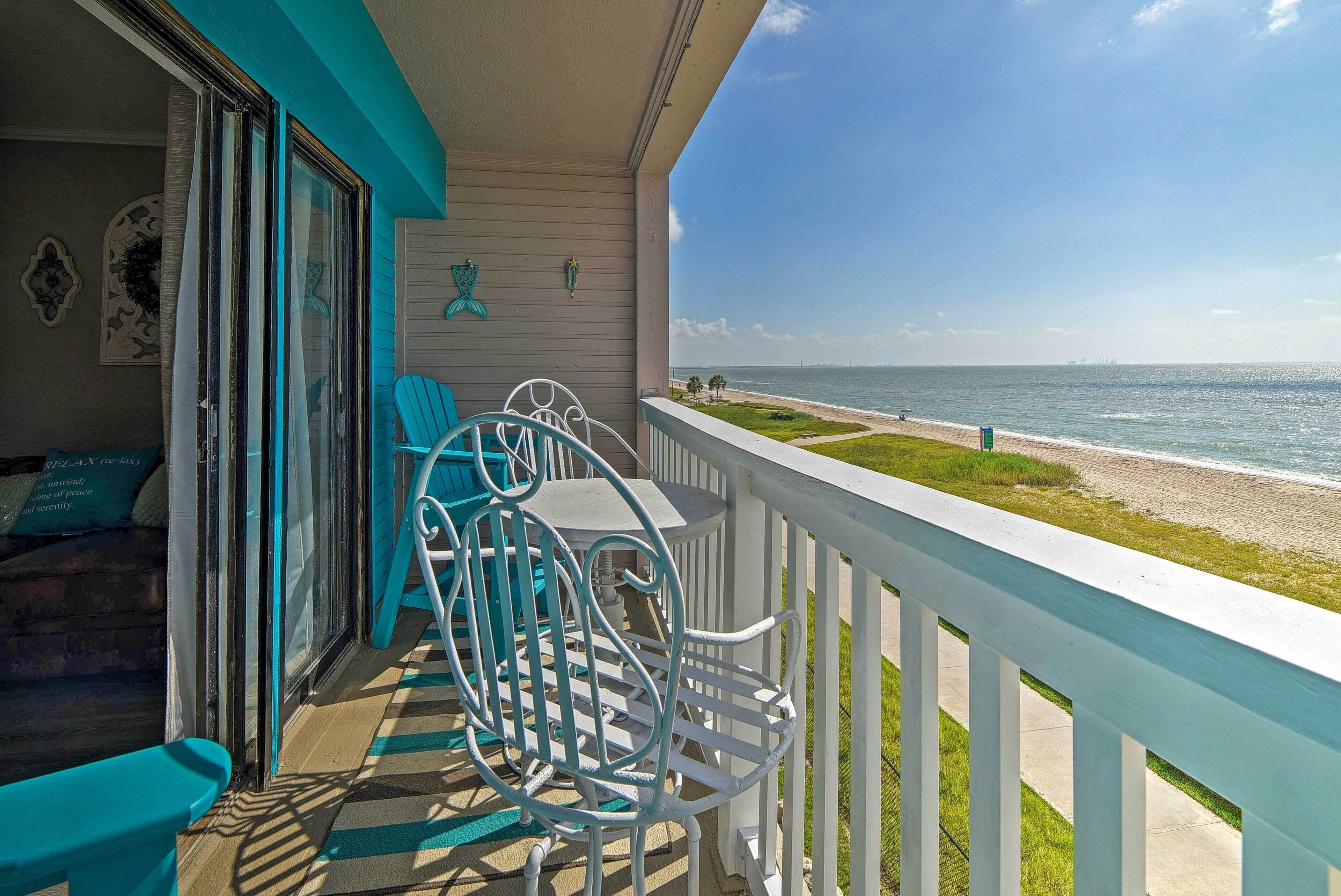 Ein Balkon mit Blick auf den Strand, ein Tisch mit Stühlen und eine Tür zu einem Zimmer.
