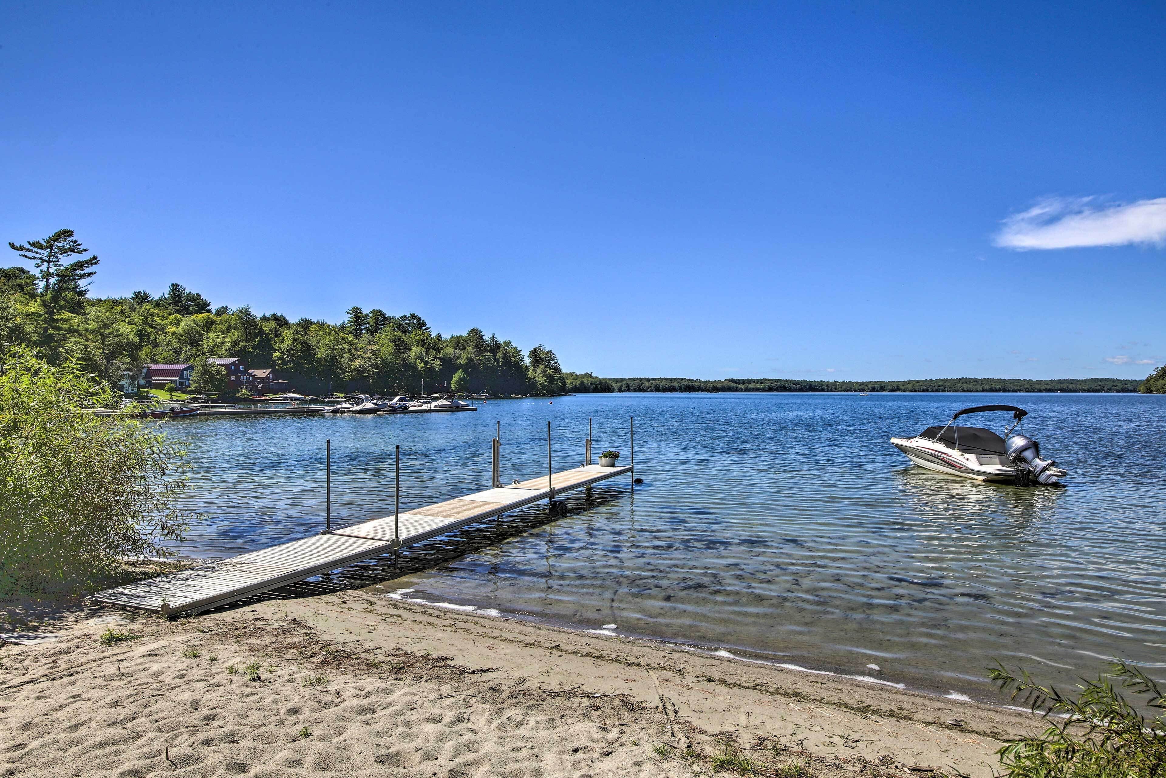 A clear lake with a wooden dock extending into the water, a boat on the right, and a forested shoreline.