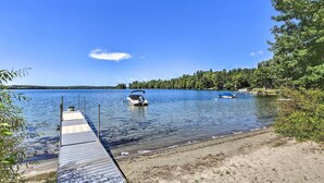 A wooden dock extending into a calm lake with boats anchored nearby. - Quaint Oakland Getaway on East Pond Lake! (Oakland)
