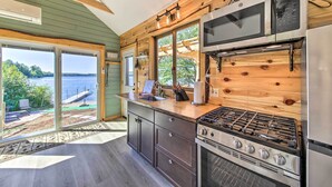 A modern kitchen with a large stove, microwave, and refrigerator. It features wooden walls and large windows overlooking a body of water. - Quaint Oakland Getaway on East Pond Lake! (Oakland)