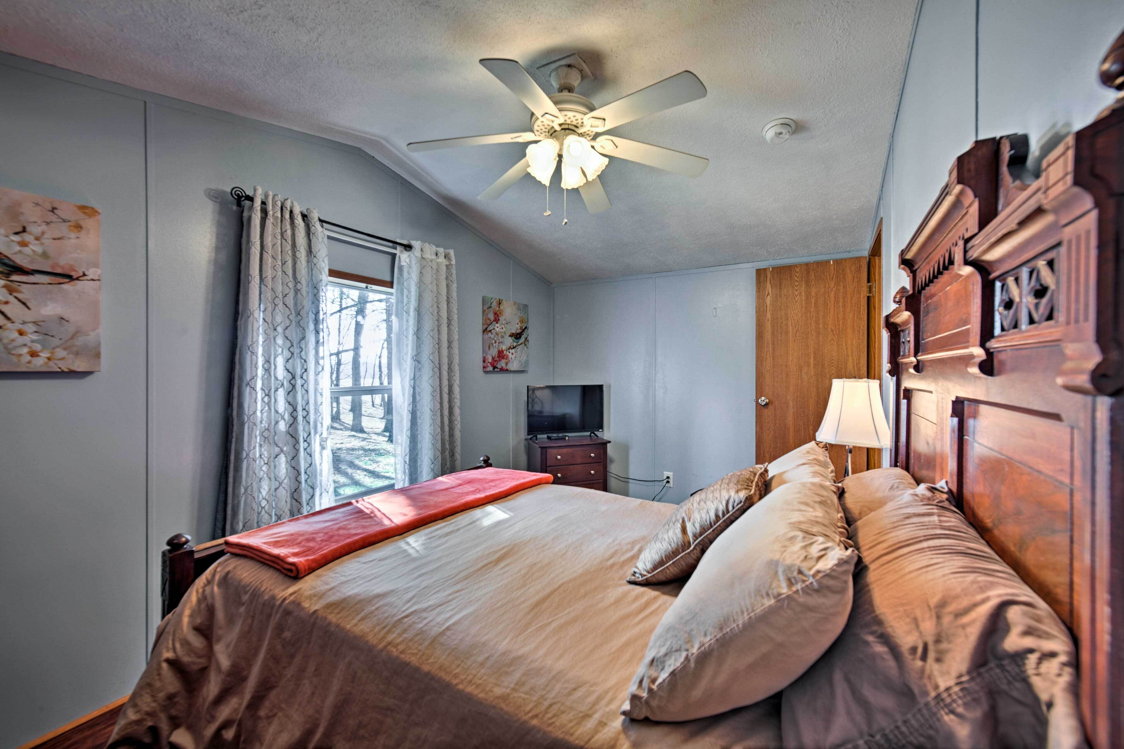 A bedroom with a bed, a ceiling fan, a TV, a wooden wardrobe, and a window with curtains.