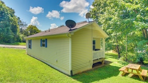 A small yellow cabin with satellite dishes on the roof, a porch, and a picnic table in a grassy area. - Walk to Main St: Inviting Byrdstown Home w/ Yard! (Byrdstown)