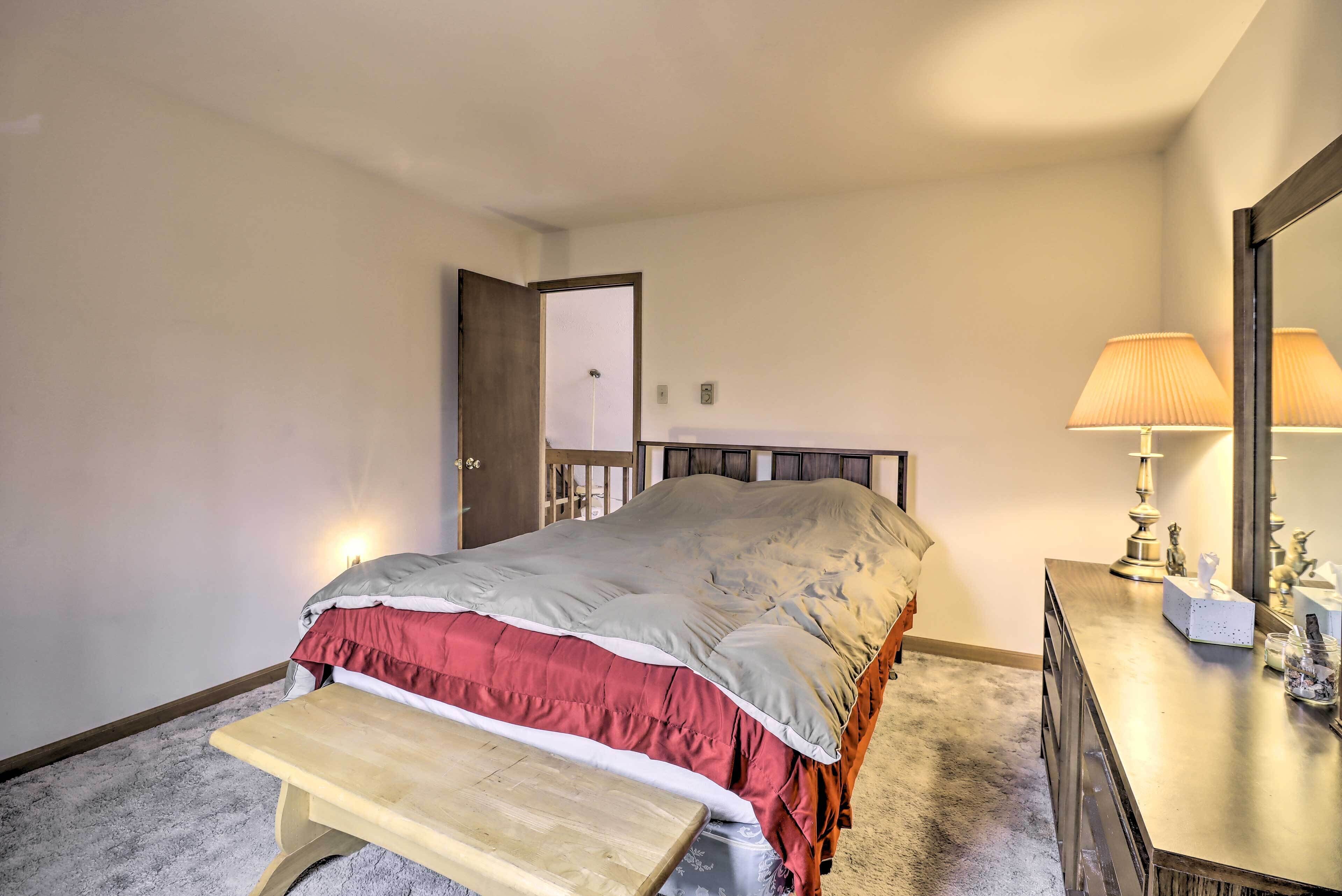 A bedroom with a bed, a bench, a dresser, a lamp, and a mirror.