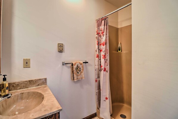 A bathroom with a beige sink, a towel rack with a decorative towel, a shower curtain with a floral pattern, and a bottle of shampoo on the wall. - ~ 1 Mi to Lake: Secluded Poconos Home w/ Decks (Jim Thorpe)