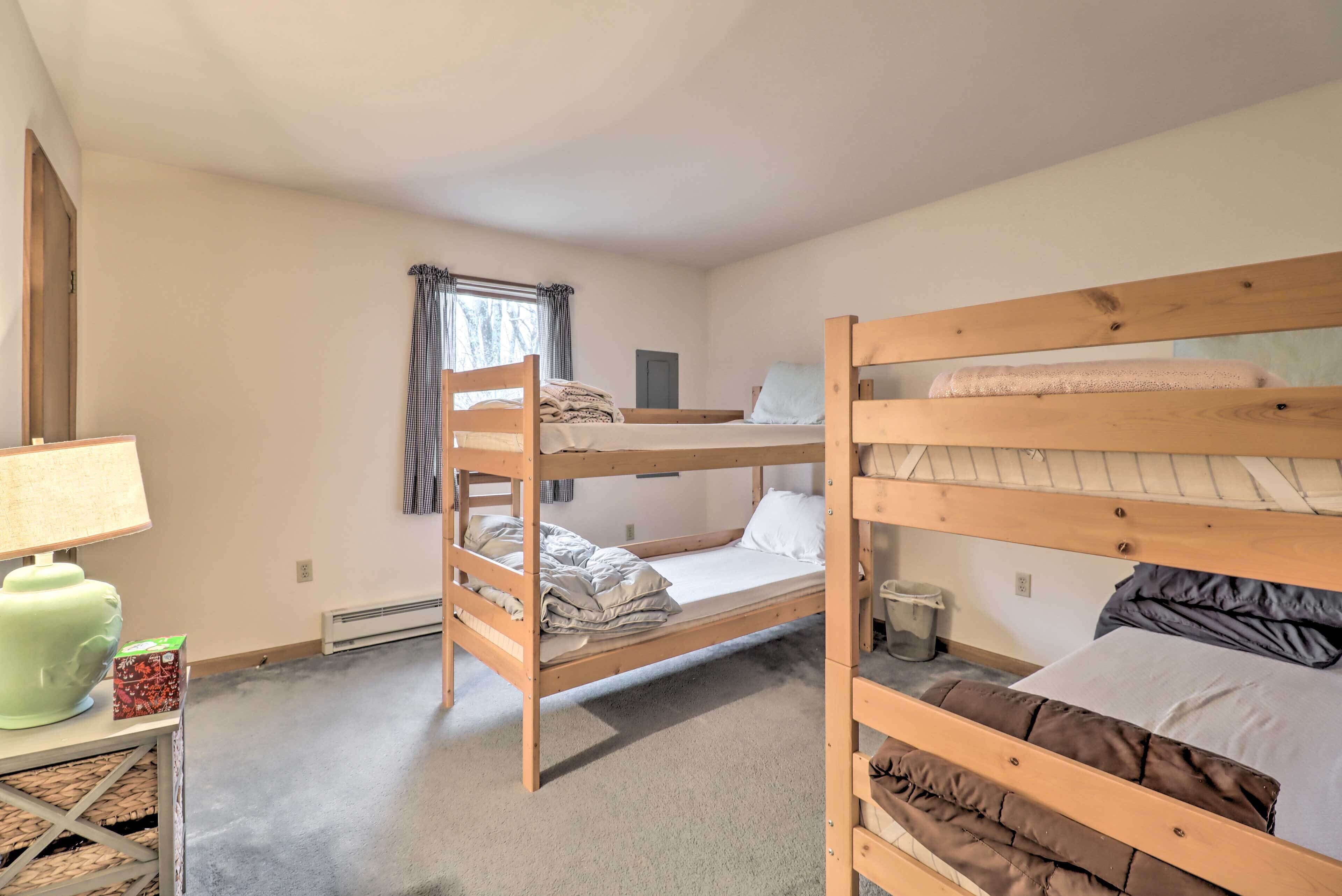 A dormitory room with bunk beds, a small table with a lamp, and a window with curtains.