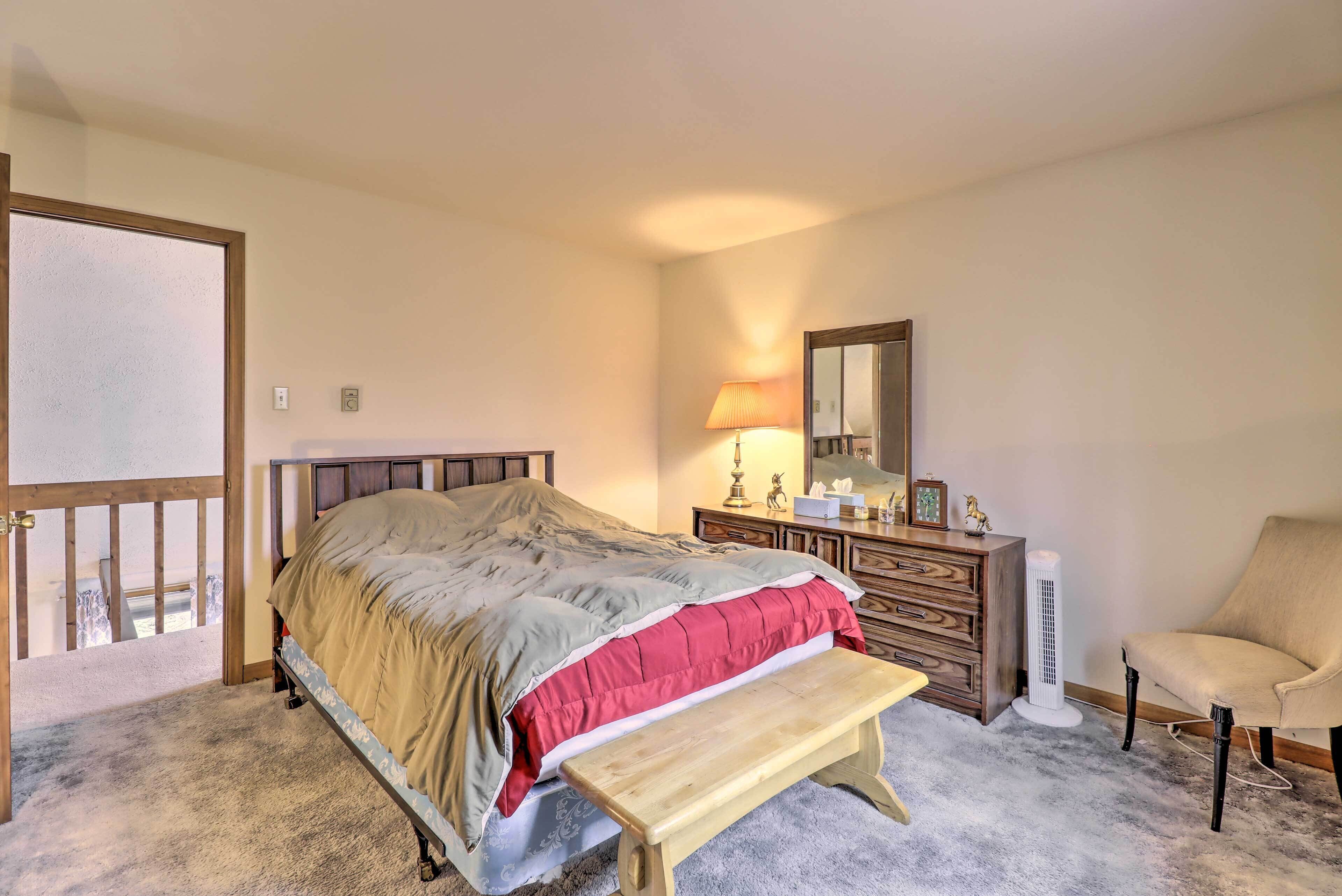 A bedroom with a bed, a wooden bench, a dresser, a chair, and a standing heater.