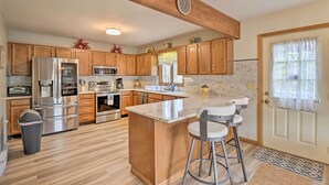 A kitchen with wooden cabinets, stainless steel appliances, a large island with bar stools, and a clock on the wall. - ~ 1 Mi to Lake: Secluded Poconos Home w/ Decks (Jim Thorpe)