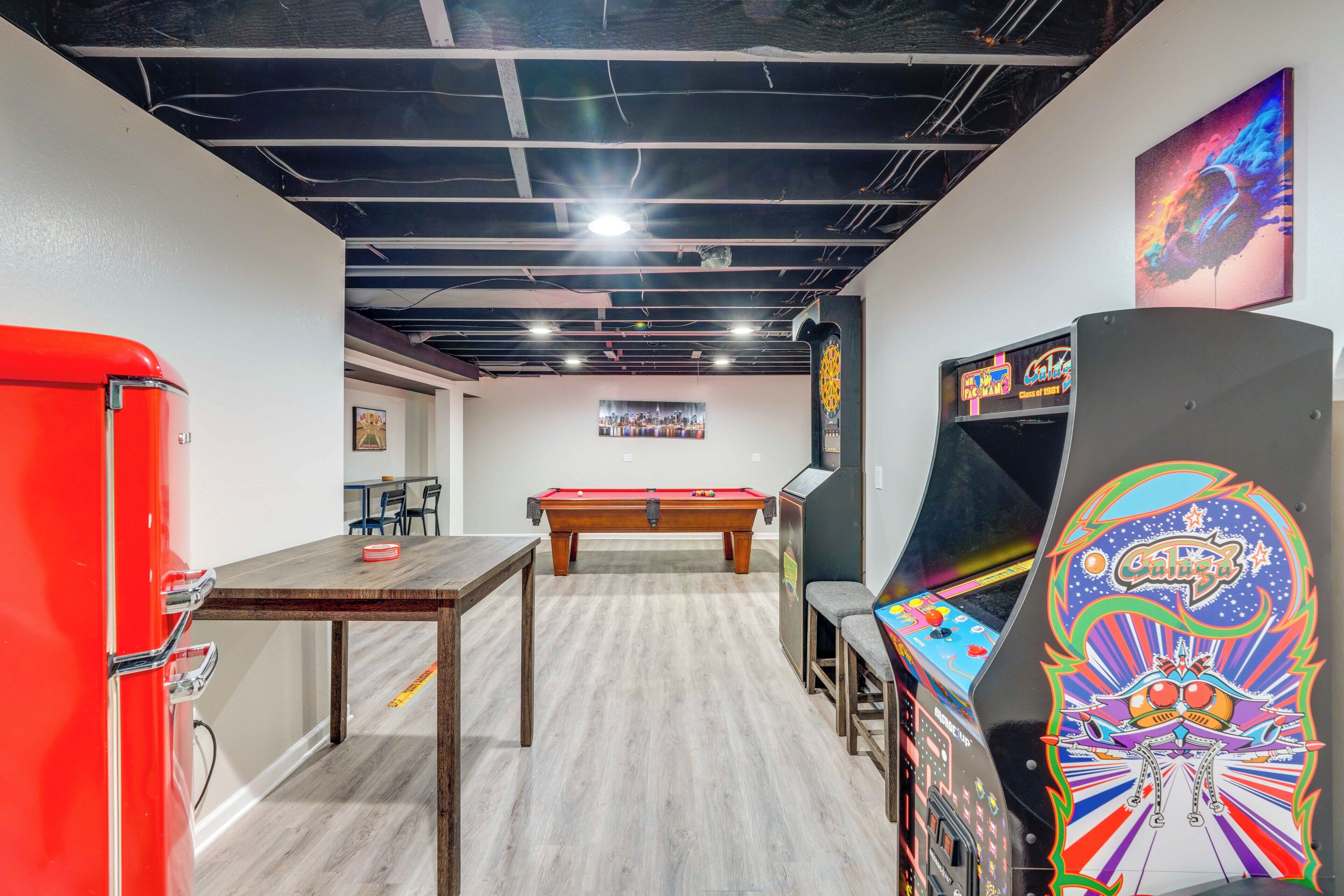 Une pièce avec une table de billard, un réfrigérateur rouge et un flipper.