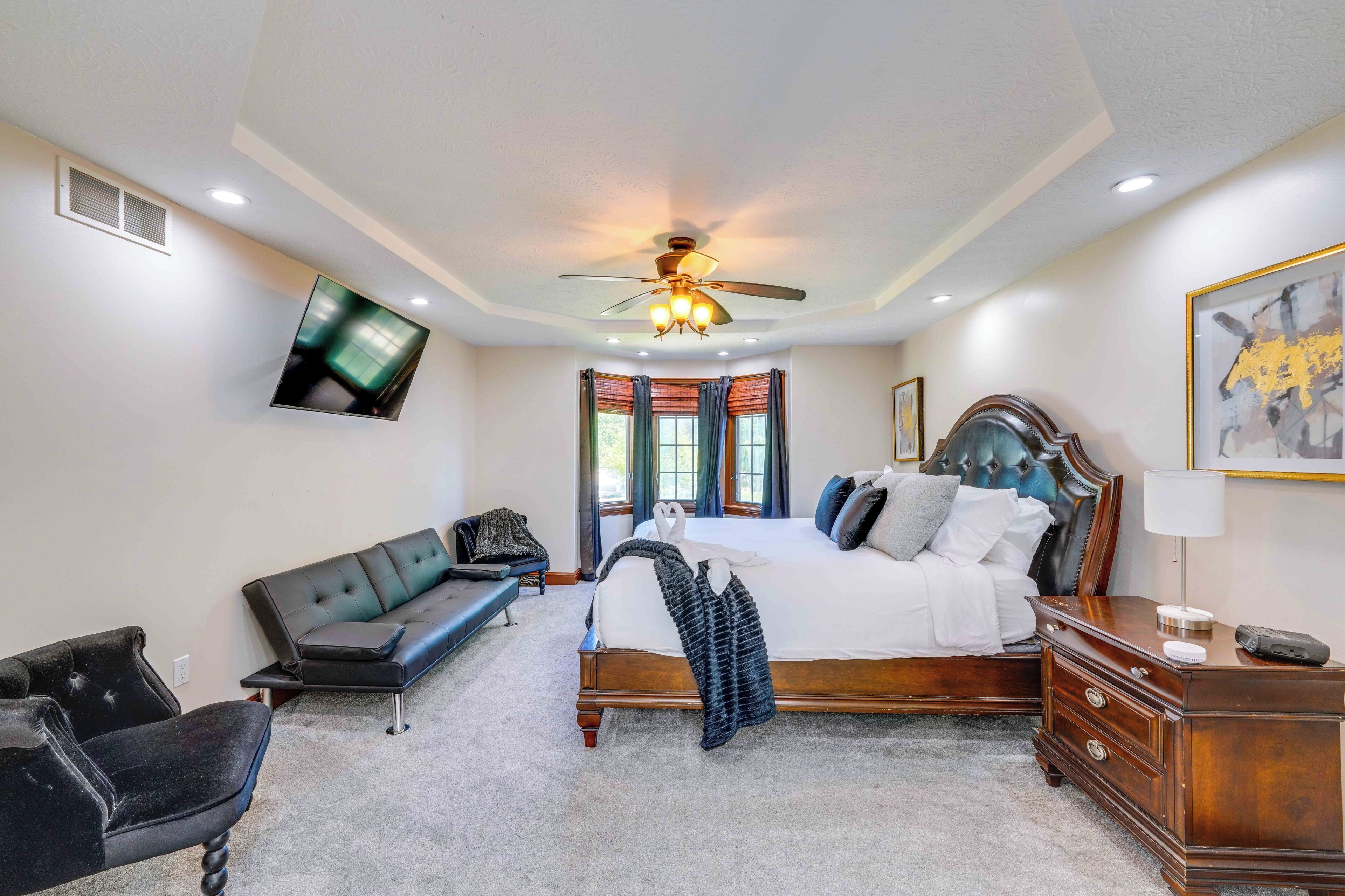 A bedroom with a bed, a ceiling fan, a TV, a bench, and a nightstand.