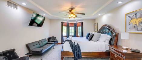 A bedroom with a bed, a ceiling fan, a TV, a bench, and a nightstand.