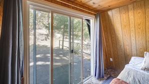 A room with a large sliding glass door leading to an outdoor area, wooden walls, and a bed with pillows. - Quiet Sequoia National Forest Cabin w/ Fireplace (Posey)