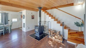 A spacious living area with a wooden floor, a built-in wood stove, a staircase, and a dining area with chairs and a table. - Quiet Sequoia National Forest Cabin w/ Fireplace (Posey)