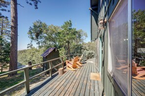 Una terraza de madera con mecedoras y un cobertizo pequeño, rodeada de árboles.