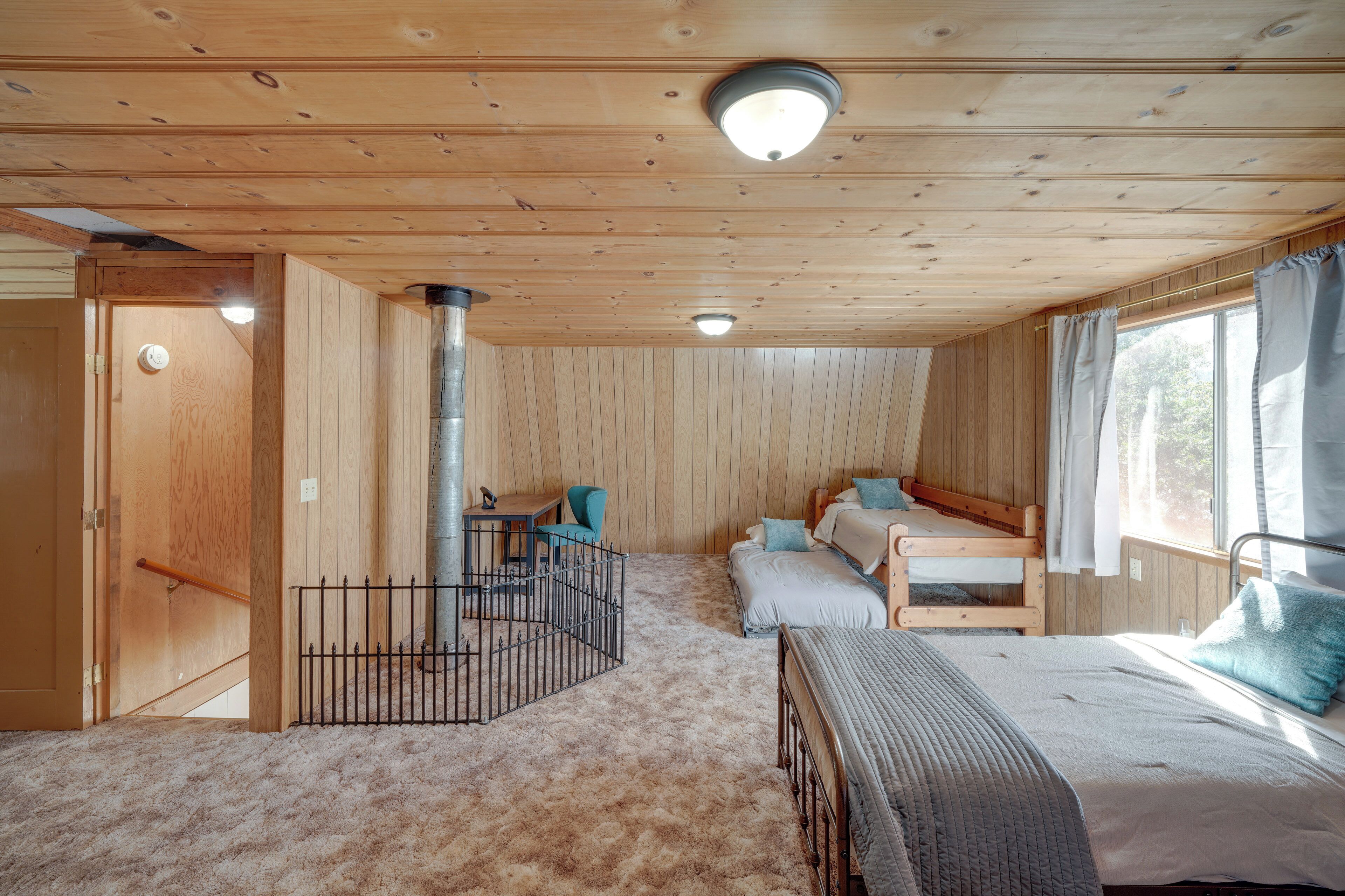 A cabin interior with a wooden ceiling, a bunk bed, a desk, and a window with curtains.