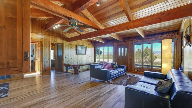 A spacious living room with wooden floors, a ceiling fan, and large windows offering a view of the outdoors. - Spacious Pinedale Home w/ Mountain Range View (Pinedale)