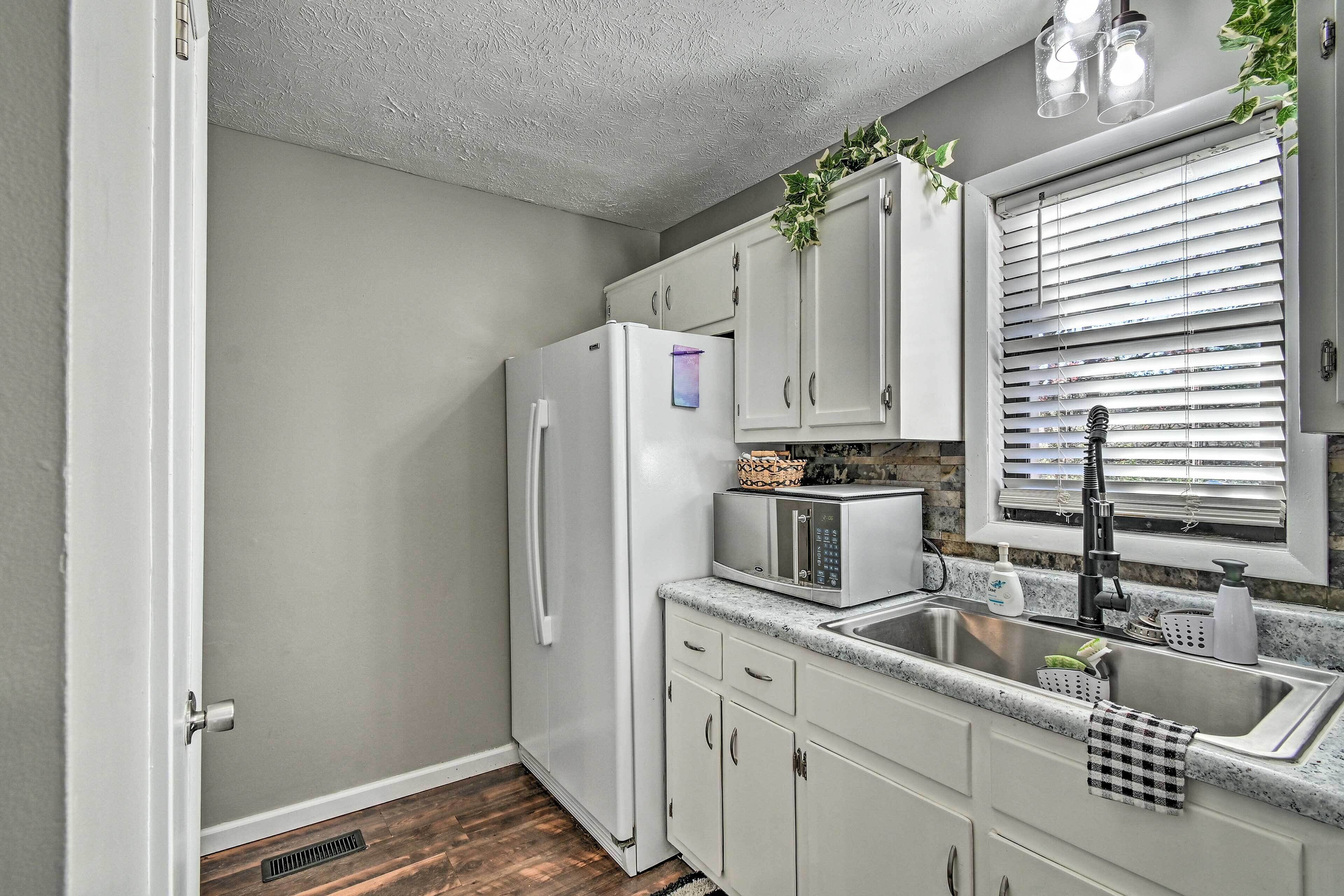 A kitchen with white cabinets, a stainless steel refrigerator, a microwave, and a sink with a faucet.