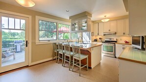 A kitchen with a central island, white cabinets, and a view of the outdoors through large windows. - Southwest Harbor Home-3 Min to Acadia Natl Park (Southwest Harbor)