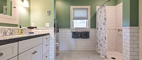 A bathroom with a white tiled floor, a shower area with a patterned shower curtain, and a window with blinds.