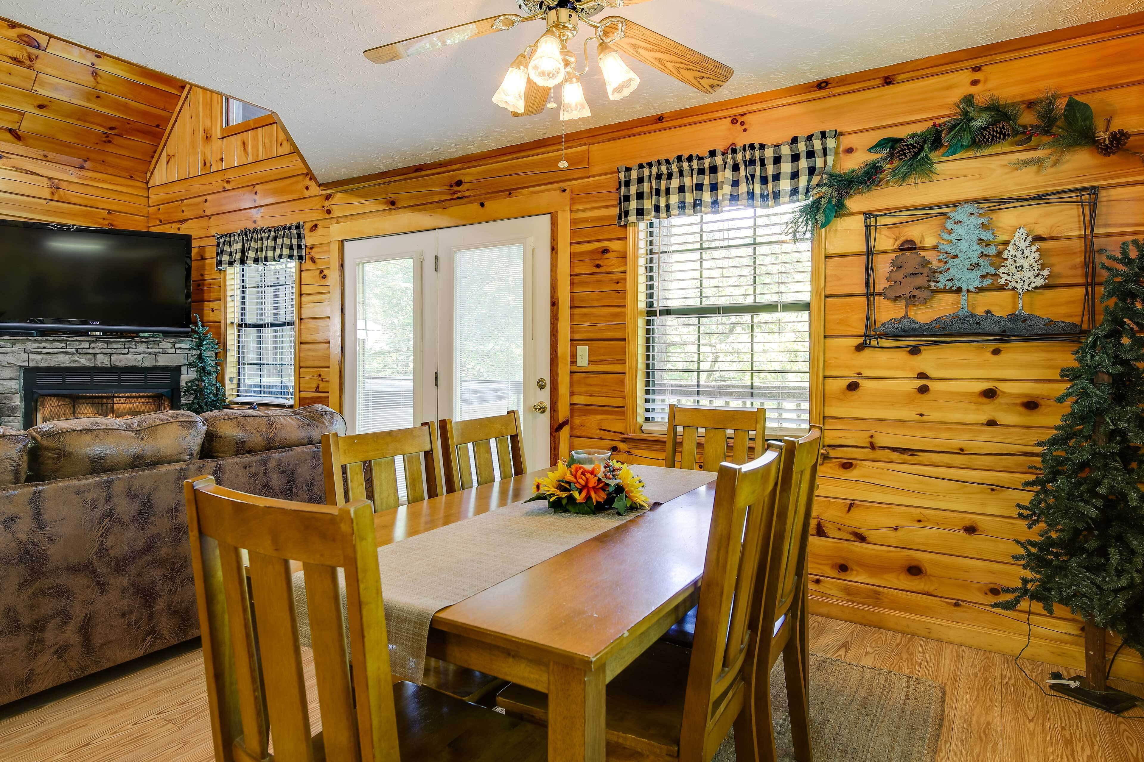 L’intérieur chaleureux d’un chalet comprend une table à manger, des chaises, un canapé, une cheminée et un téléviseur.