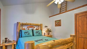 Quarto rústico com estrutura de cama de madeira, colcha azul com motivos de cavalos, mesa de cabeceira pequena com abajur e cabeceira de madeira.