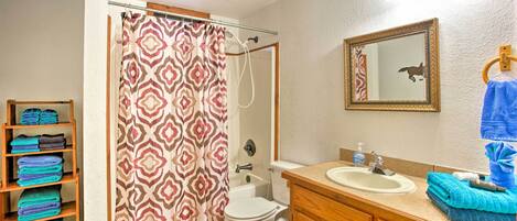 A bathroom with a shower curtain, toilet, sink, and a towel rack with towels.