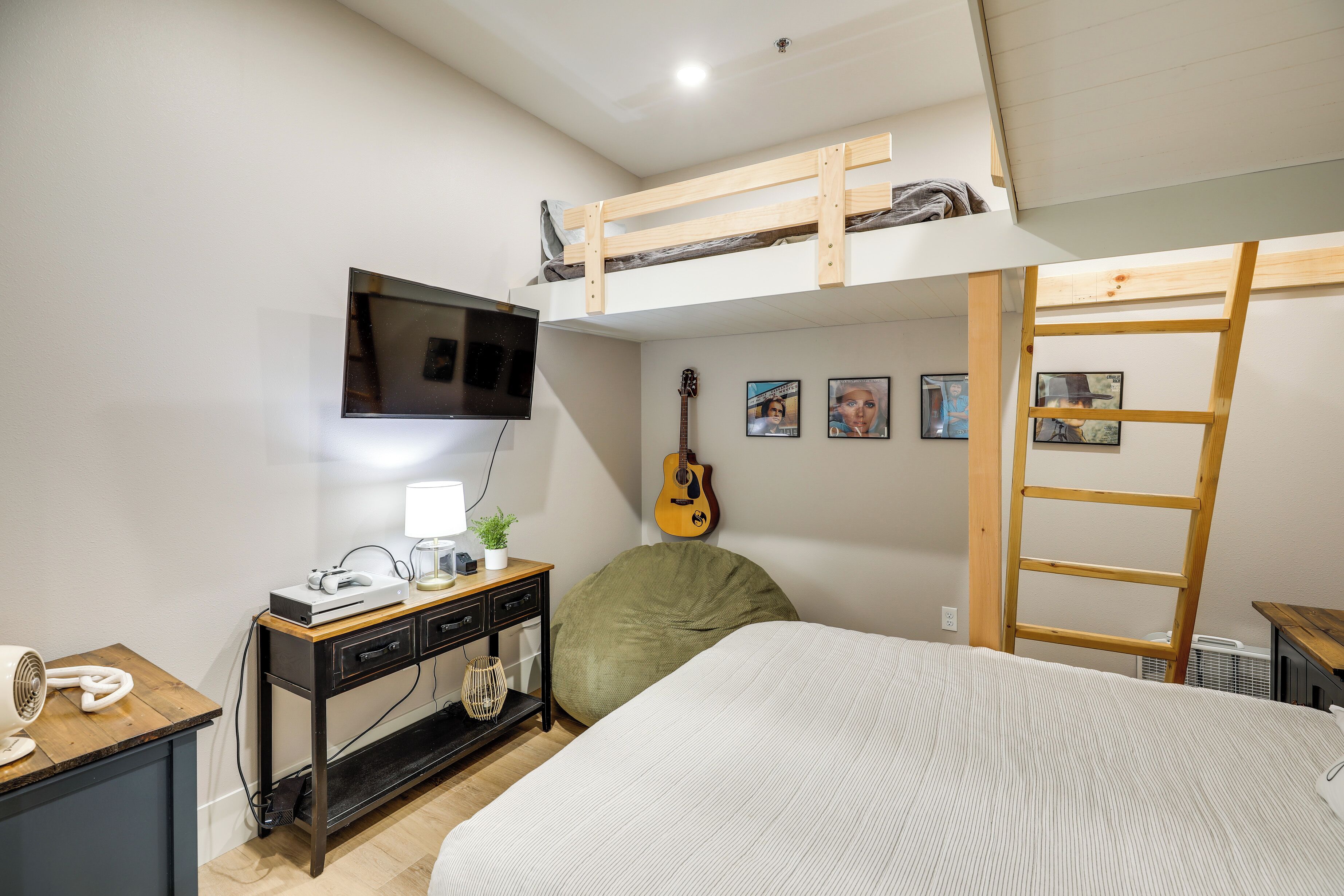 Una camera da letto con un letto a castello, una scrivania con computer e lampada, una chitarra e una scala.